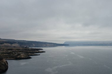 Mavi-gri ölçekte güzel sisli bir manzara: ufukta koyu mavi dağlar, kuru çimlerle kaplı tepelerin kıyısında geniş bir nehir vardır. Colorado Nehri, OR, ABD
