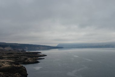 Mavi-gri ölçekte güzel sisli bir manzara: ufukta koyu mavi dağlar, kuru çimlerle kaplı tepelerin kıyısında geniş bir nehir vardır. Colorado Nehri, OR, ABD