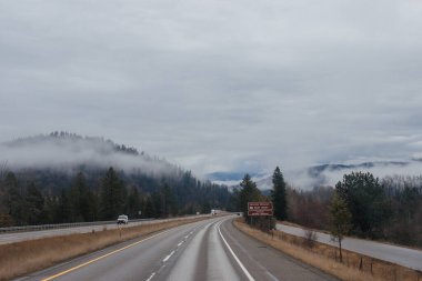 Karayolu, kışın bulutların arasında yüksek dağların arasında yol işaretleri olan, kamyon ve arabaların geçtiği yol. Idaho, ABD, 12-5-2020