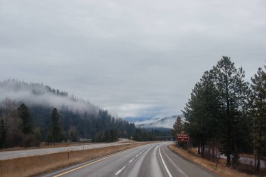 Karayolu, kışın bulutların arasında yüksek dağların arasında yol işaretleri olan, kamyon ve arabaların geçtiği yol. Idaho, ABD, 12-5-2020