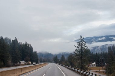 Karayolu, kışın bulutların arasında yüksek dağların arasında yol işaretleri olan, kamyon ve arabaların geçtiği yol. Idaho, ABD, 12-5-2020