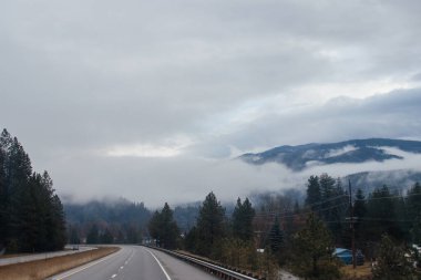 Karayolu, kışın bulutların arasında yüksek dağların arasında yol işaretleri olan, kamyon ve arabaların geçtiği yol. Idaho, ABD, 12-5-2020