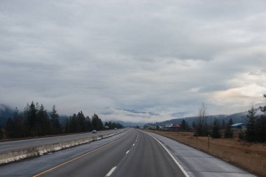 Karayolu, kışın bulutların arasında yüksek dağların arasında yol işaretleri olan, kamyon ve arabaların geçtiği yol. Idaho, ABD, 12-5-2020