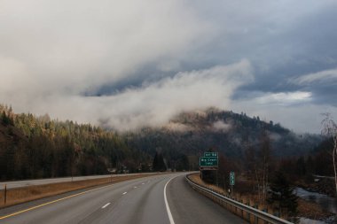 Karayolu, kışın bulutların arasında yüksek dağların arasında yol işaretleri olan, kamyon ve arabaların geçtiği yol. Idaho, ABD, 12-5-2020