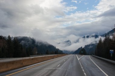 Karayolu, kışın bulutların arasında yüksek dağların arasında yol işaretleri olan, kamyon ve arabaların geçtiği yol. Idaho, ABD, 12-5-2020