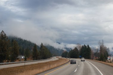 Karayolu, kışın bulutların arasında yüksek dağların arasında yol işaretleri olan, kamyon ve arabaların geçtiği yol. Idaho, ABD, 12-5-2020