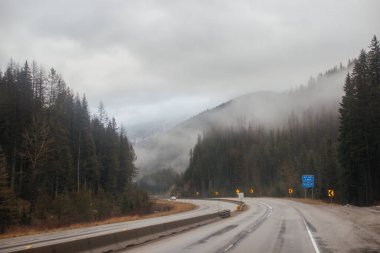 Karayolu, kışın bulutların arasında yüksek dağların arasında yol işaretleri olan, kamyon ve arabaların geçtiği yol. Idaho, ABD, 12-5-2020
