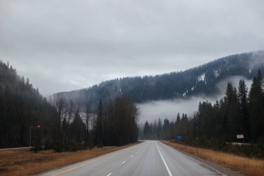 Karayolu, kışın bulutların arasında yüksek dağların arasında yol işaretleri olan, kamyon ve arabaların geçtiği yol. Idaho, ABD, 12-5-2020