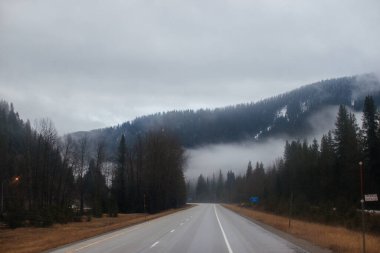 Karayolu, kışın bulutların arasında yüksek dağların arasında yol işaretleri olan, kamyon ve arabaların geçtiği yol. Idaho, ABD, 12-5-2020