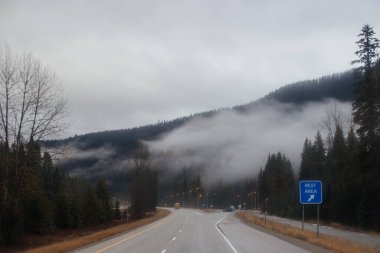 Karayolu, kışın bulutların arasında yüksek dağların arasında yol işaretleri olan, kamyon ve arabaların geçtiği yol. Idaho, ABD, 12-5-2020