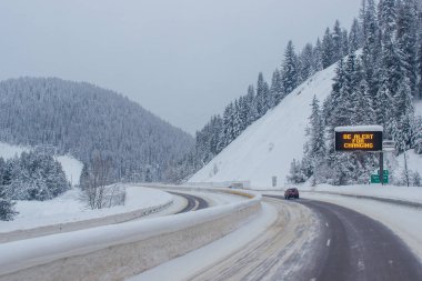Dağların arasında karla kaplı otoyol, karların arasında ağaçlar ve ağaçlar var. Karla kaplı yolu, Montana, Amerika 'daki köknar ağaçları ve dağları olan kış manzarası, 1-18-2020