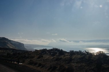 Güneşli bir günde güzel bir gündüz manzarası, güneş ışınlarında büyük bir nehir ve dağların arasında uzun bir köprü.