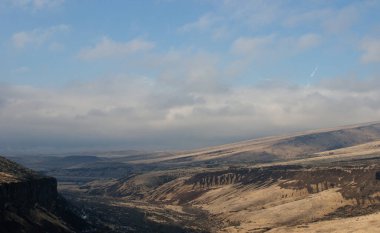 Sarı otlarla, gri-mavi bulutlarla ve yükselen bir kartalla dağlarda güzel bir manzara.