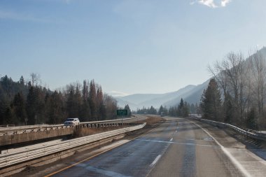 Arabaların ve kamyonların gittiği asfalt bir yol, dağların arasında, ufukta sisli dağlar, gökyüzü bulutlarla kaplı. Idaho, ABD, 11-23-2019
