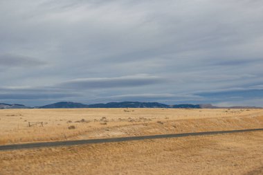 Bozkırların arasında asfalt yol, sarı kuru çimenler ufukta mavi dağlar, güzel mavi-gri sonbahar gökyüzü. Montana, ABD, 11-23-2019