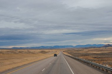 Bozkırların arasında asfalt yol, sarı kuru çimenler ufukta mavi dağlar, güzel mavi-gri sonbahar gökyüzü. Montana, ABD, 11-23-2019