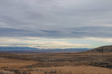 Bozkırların arasında asfalt yol, sarı kuru çimenler ufukta mavi dağlar, güzel mavi-gri sonbahar gökyüzü. Montana, ABD, 11-23-2019