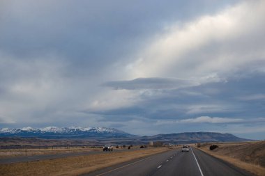 Sonbahar manzarası alacakaranlıkta. Bozkırların arasında asfalt yol, sarı kuru çimenler ufukta mavi dağlar, güzel mavi-gri sonbahar gökyüzü. Montana, ABD, 11-23-2019