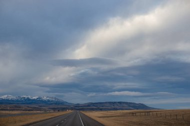 Sonbahar manzarası alacakaranlıkta. Bozkırların arasında asfalt yol, sarı kuru çimenler ufukta mavi dağlar, güzel mavi-gri sonbahar gökyüzü. Montana, ABD, 11-23-2019