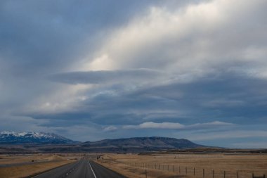 Sonbahar manzarası alacakaranlıkta. Bozkırların arasında asfalt yol, sarı kuru çimenler ufukta mavi dağlar, güzel mavi-gri sonbahar gökyüzü. Montana, ABD, 11-23-2019