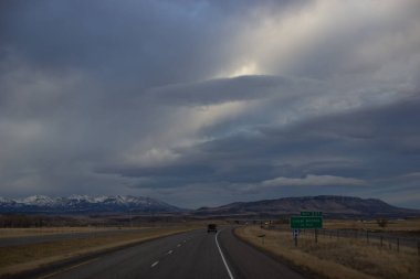 Sonbahar manzarası alacakaranlıkta. Bozkırların arasında asfalt yol, sarı kuru çimenler ufukta mavi dağlar, güzel mavi-gri sonbahar gökyüzü. Montana, ABD, 11-23-2019