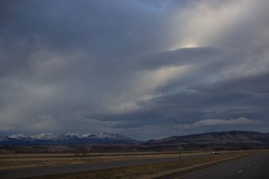 Sonbahar manzarası alacakaranlıkta. Bozkırların arasında asfalt yol, sarı kuru çimenler ufukta mavi dağlar, güzel mavi-gri sonbahar gökyüzü. Montana, ABD, 11-23-2019
