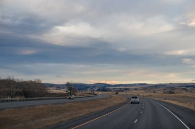 Sonbahar manzarası alacakaranlıkta. Bozkırların arasında asfalt yol, sarı kuru çimenler ufukta mavi dağlar, güzel mavi-gri sonbahar gökyüzü.