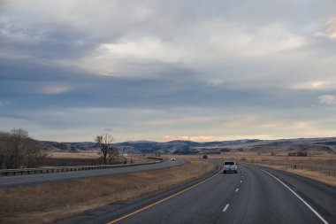 Sonbahar manzarası alacakaranlıkta. Bozkırların arasında asfalt yol, sarı kuru çimenler ufukta mavi dağlar, güzel mavi-gri sonbahar gökyüzü.