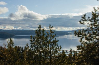 Büyük gölü olan güzel bir manzara, gölü çevreleyen mavi dağlar, açık mavi gökyüzü ve güneş.