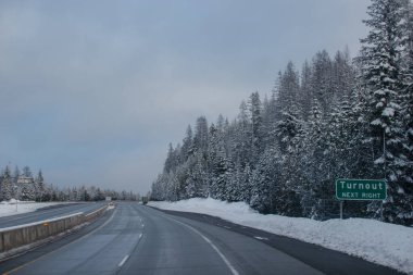 Gün batımında karla kaplı dağlar ve yüksek köknar ağaçları arasında kış karayolu.