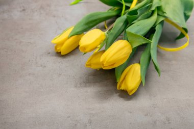 Gri desenli arka planda, koyu gri mermer üzerinde güzel sarı laleler. Gri arka planda yeşil yapraklı bir buket sarı çiçek. Sarı-gri-yeşil buket.