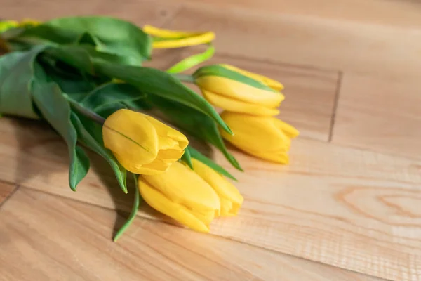 Beautiful yellow tulips on a wooden textured background, on a parquet. A bouquet of yellow flowers with green leaves on parquet boards. Spring yellow-green bouquet.