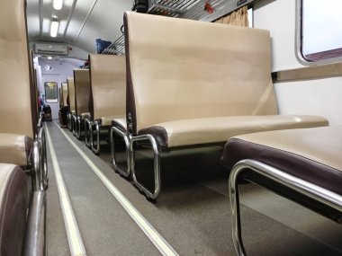 Boş ekonomi sınıfı bir tren vagonunun içi, bej koltuklar, koridor ve genel depo alanlarını gösteren bir bakış açısı..