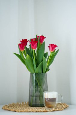 Cam vazoda kırmızı laleler, Beyaz Masa 'da kahve fincanı, iç kısımda da rahat.