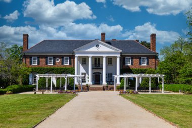 Ziyaretçiler büyüleyici beyaz pergolaların altındaki banklarda dinlenerek görkemli tuğlalı bir malikanenin manzaralı bahçesinin tadını çıkarıyorlar. Bu tarihi konak, büyük beyaz sütunlu portosu ve titizlikle peyzajlanmış bahçeleriyle çok güzel bir ortam sunuyor.