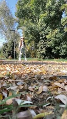 8 yaşındaki neşeli bir kız, renkli yapraklarla dolu bir sonbahar parkında paten kayıyor. Kask ve koruyucu giysiler giyerek aktif ve neşeli bir açık hava gününün tadını çıkarıyor..