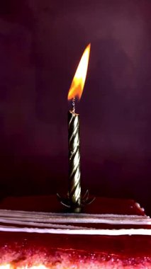 Kırmızı katmanlı tatlı dilimi ve altın kaplama bir tabakta yanan bir doğum günü mumu. Ilık, ışıl ışıl ve gül kırmızısı arka plan neşeli, samimi bir kutlama havası yaratır..