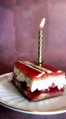 Kırmızı katmanlı tatlı dilimi ve altın kaplama bir tabakta yanan bir doğum günü mumu. Ilık, ışıl ışıl ve gül kırmızısı arka plan neşeli, samimi bir kutlama havası yaratır..