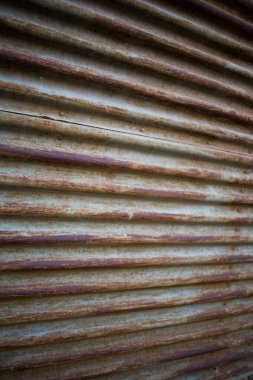 Açık gri boya ve koyu kahverengi ve turuncu tonlarda ağır pas içeren kıvrımlı metalin açılı yakın çekimi. Yaşlanma, aşınma ve yıpranmış yüzey derinliğini gösteren güçlü endüstriyel doku..