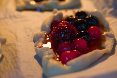 Ahududu, yaban mersini ve yabanmersinli meyveli turta yakın plan. Yumuşak ışık parlak kabukları ve sulu böğürtlenleri ön plana çıkarır, samimi ve davetkar bir pişirme havası yaratır..