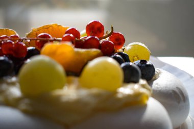 Pavlova kremalı tatlı ve kırmızı frenk üzümü, yabanmersini ve narenciye dilimleri de dahil olmak üzere taze böğürtlenler. Parlak yönlü ışık dokuları ve renkleri güçlendirir.