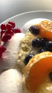 Pavlova kremalı tatlı ve kırmızı frenk üzümü, yabanmersini ve narenciye dilimleri de dahil olmak üzere taze böğürtlenler. Parlak yönlü ışık dokuları ve renkleri güçlendirir.