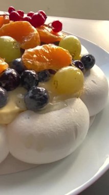 Pavlova kremalı tatlı ve kırmızı frenk üzümü, yabanmersini ve narenciye dilimleri de dahil olmak üzere taze böğürtlenler. Parlak yönlü ışık dokuları ve renkleri güçlendirir.