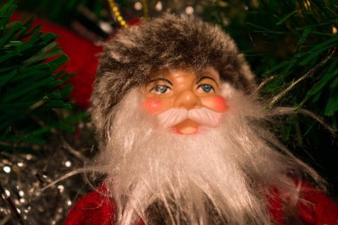 Noel ağacında asılı büyüleyici bir Noel Baba süsü. Detaylı tekstil kıyafetleri, kabarık şapkalar ve yumuşak sıcak tatil ışıklandırması..