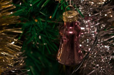 Yeşil iğneler ve gümüş süslemelerle çevrili, altın kaplamalı, metalik, pembe bir Noel süsü. Muhteşem bir bayram görüntüsü için ışığı yansıtıyor..