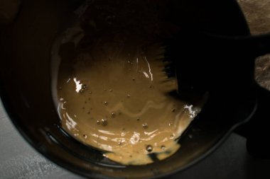 Siyah bir kâsede saç boyası karışımı ve profesyonel boya fırçası. Yumuşak ışık, koyu arkaplan ve kurutulmuş pampa otları ile kremsi bej rengi, sakin bir salon atmosferi yaratıyor..