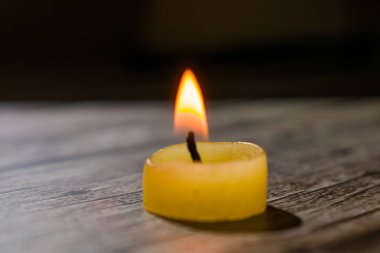 Üçgen şeklinde dizilmiş yanan mumların yakın çekimi. Koyu bir zemin, yumuşak bir alan derinliği ve şeffaf bir balmumu ile parlak alevler kontrastı samimi, atmosferik bir sahne yaratıyor..