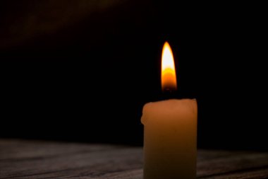 Üçgen şeklinde dizilmiş yanan mumların yakın çekimi. Koyu bir zemin, yumuşak bir alan derinliği ve şeffaf bir balmumu ile parlak alevler kontrastı samimi, atmosferik bir sahne yaratıyor..