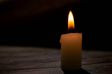 Üçgen şeklinde dizilmiş yanan mumların yakın çekimi. Koyu bir zemin, yumuşak bir alan derinliği ve şeffaf bir balmumu ile parlak alevler kontrastı samimi, atmosferik bir sahne yaratıyor..