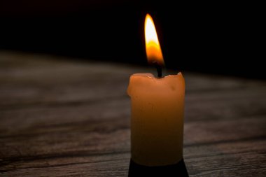 Üçgen şeklinde dizilmiş yanan mumların yakın çekimi. Koyu bir zemin, yumuşak bir alan derinliği ve şeffaf bir balmumu ile parlak alevler kontrastı samimi, atmosferik bir sahne yaratıyor..